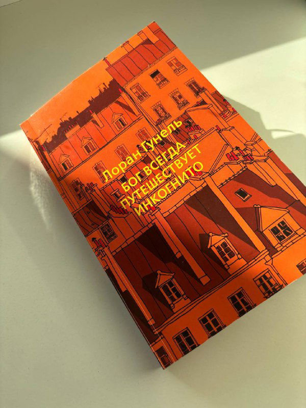 Оранжевая обложка Лорана Гунеля «Бог всегда путешествует инкогнито» снята под углом на светлом фоне; видна архитектурная иллюстрация.