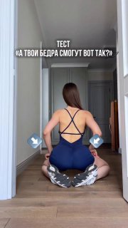 Женщина в синем спортивном костюме сидит на пятках и разводит колени в стороны — демонстрация теста на подвижность тазобедренных суставов в квартире, ракурс сзади.