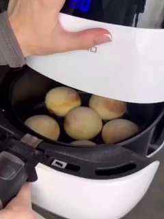 Кадр: рука приподнимает крышку аэрогриля, внутри несколько круглых золотистых сырников — этап приготовления из видео, показывающий готовку в приборе.