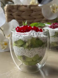 Стеклянный десерт из чиа с кусочками киви и ягодами сверху, сервированный в двухслойном стакане‑кубке на светлом фоне.