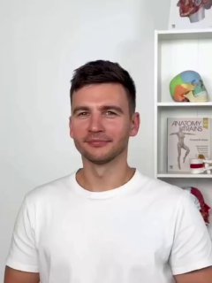 Кадр из видео: мужчина‑инструктор в белой футболке на фоне анатомических моделей и плакатов демонстрирует упражнение для расслабления височной мышцы и подтяжки лица.