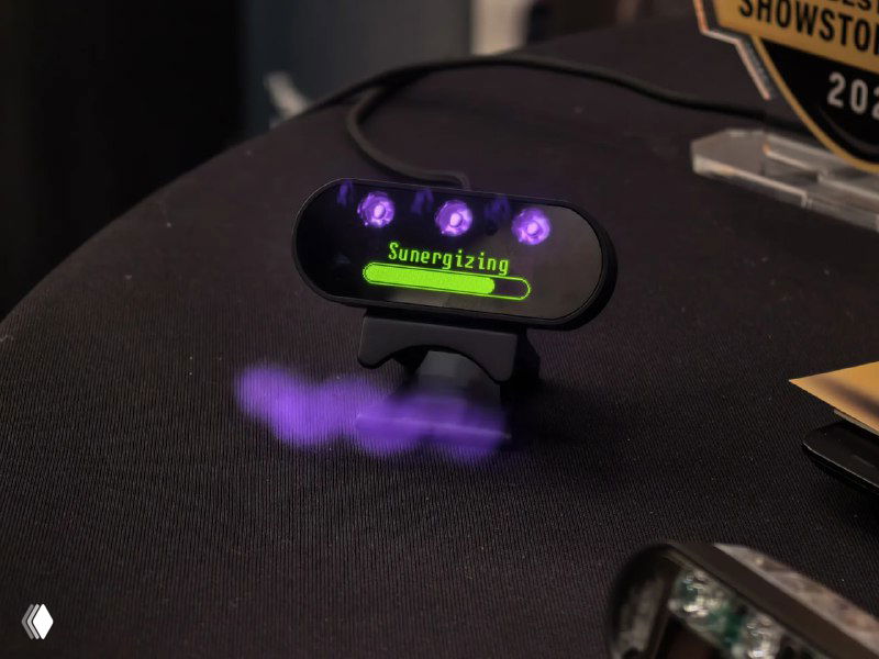 Крупный план устройства SunBooster с фиолетовыми светодиодами и зелёной надписью на экране, видно свечение и элементы управления на демонстрации.