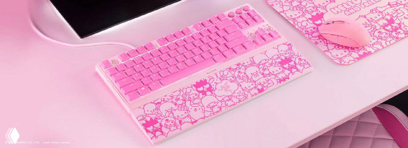 Розовая клавиатура, мышь и коврик с принтом Hello Kitty расположены на столе — геймерская периферия в пастельных тонах.
