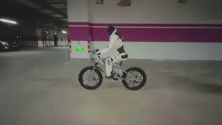 Фотография гуманоидного робота Lingxi X2, едущего на велосипеде в подземном паркинге; робот в белом корпусе держит равновесие и крутит педали в тестовом заезде.