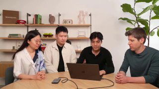 Группа из четырёх человек вокруг ноутбука в студии: демонстрация функционала, разговор и обмен идеями на фоне полок и растений.