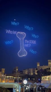 Световое изображение косточки и текстовых надписей в небе, выполненное дронами в ходе шоу — ночной городской фон и огни.