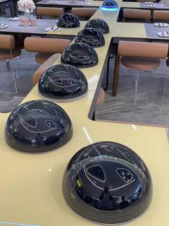 Внутренний вид ресторана в стиле НЛО: ряд круглых чёрных автономных модулей «летающих тарелок» на столах, предназначенных для доставки блюд посетителям