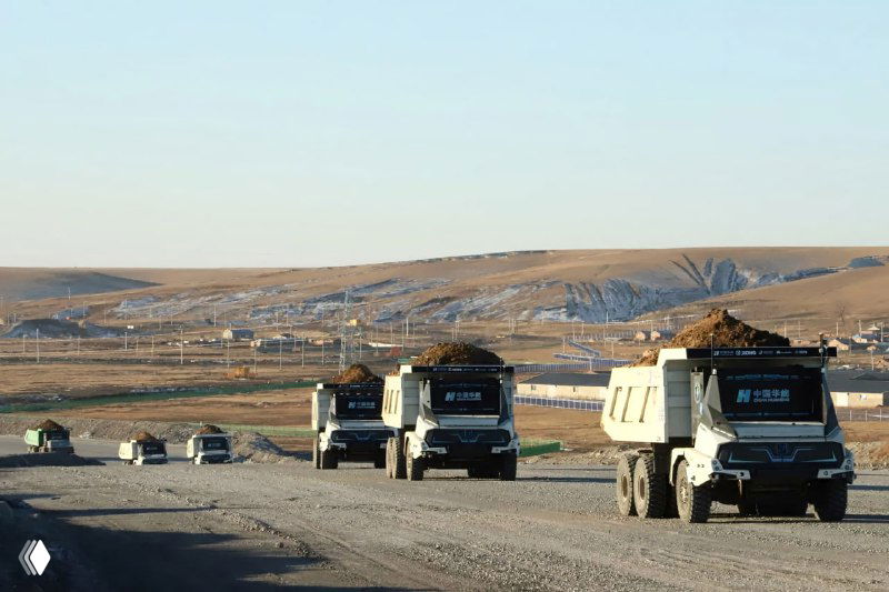 Равнинный участок карьера с движущимися автономными грузовиками, несколько машин в рамках маршрута перевозки горной массы.