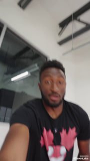 Размытое селфи мужчины в тёмной футболке, снятое в офисном интерьере; видны потолочные балки и светильник, кадр сделан с руки.