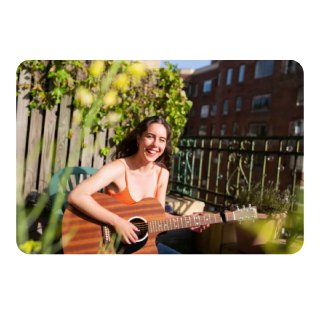 Пример обработанной фотографии: улыбающаяся девушка с гитарой на балконе — демонстрация улучшений цвета и боке после ИИ‑редактирования.