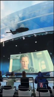 Кадр с проекции «Матрицы» на дуговом экране и силуэт вертолёта в верхней части кадра — вид интерьера иммерсивного пространства с сидящими зрителями.