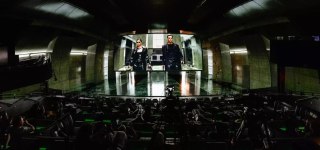 Финальный панорамный снимок зала Cosm: широкий изогнутый экран показывает сцены фильма, зрители сидят в амфитеатре, атмосфера иммерсивного показа.