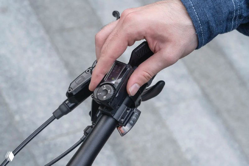 Рука управляет пультом на руле велосипеда; видны кнопки и регулятор скорости, интерфейс для блокировки через приложение.