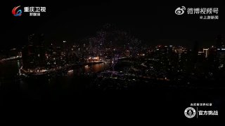 Ночной вид городского побережья с огнями и началом масштабного дрон-шоу в Китае; кадр с логотипом телекомпании и городской подсветкой.