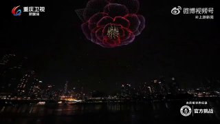 Крупный план световой композиции из дронов, формирующей цветок‑похожую структуру на фоне ночного неба и огней города.