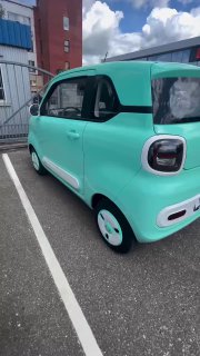 Вид сбоку на мятно-голубой микрокар Bestune Pony, подчёркнута компактность, двери и небольшие диски на фоне городского стояночного места.