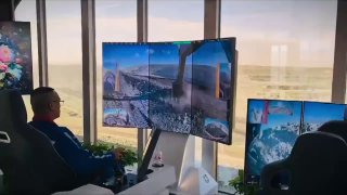 Оператор BuilderX в офисе за большим изогнутым монитором, на экране панорама стройплощадки и вид с экскаватора, пульт управления рядом.