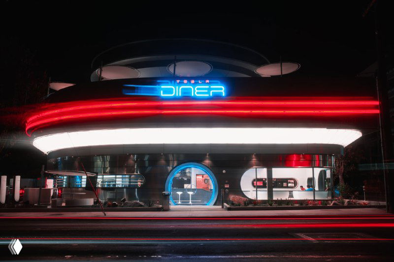 Фасад Tesla Diner с неоновым знаком DINER: витрины, вход и ночная улица перед зданием — атмосферный кадр ретрозакусочной будущего.