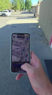 Рука держит смартфон с картой и приложением автопарковки на фоне переоборудованного Ford Mustang — демонстрация работы автопилота и навигации