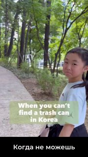 Девочка стоит на дорожке в парке Сеула среди густых деревьев; на фото видна англоязычная надпись про поиск урны в Корее.