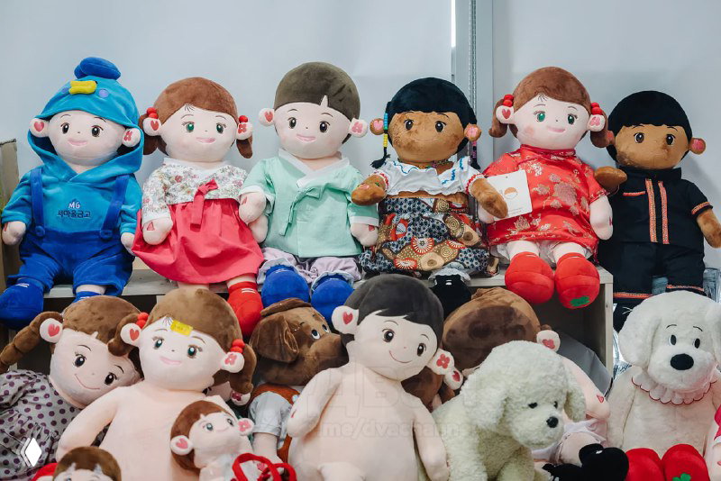 Ряд мягких игрушек‑кукол Hyodol разных моделей и цветов, выставленных на полке — демонстрация модельного ряда и массового производства.