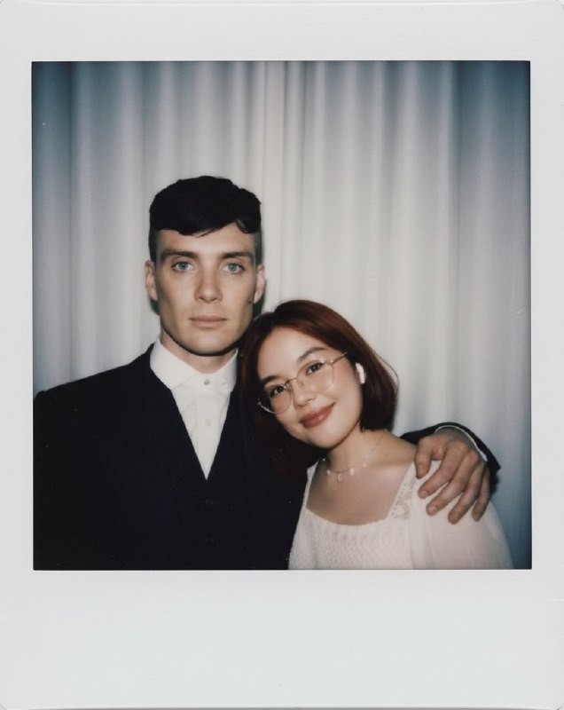 Полароидный кадр двоих людей в полу‑анфас на фоне простой занавески; атмосферный мягкий свет и ощущение спонтанного снимка без постановки.