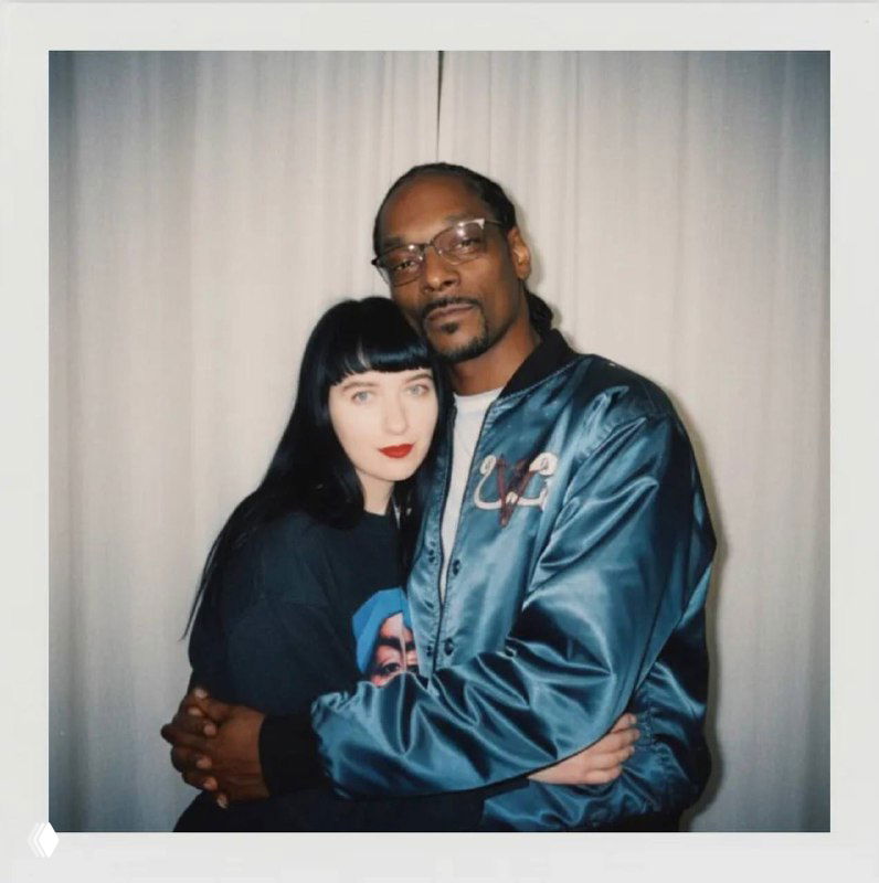 Полароидный снимок пары в объятиях: темнокожий мужчина и женщина в контрастном свете, нейтральный фон‑занавеска и мягкая подсветка вспышки.