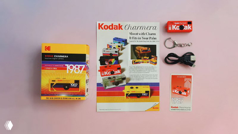 Распакованный комплект Kodak Charmera: коробка, буклет, миниатюрный брелок-камера и аксессуары на столе, показывающие компактность продукта