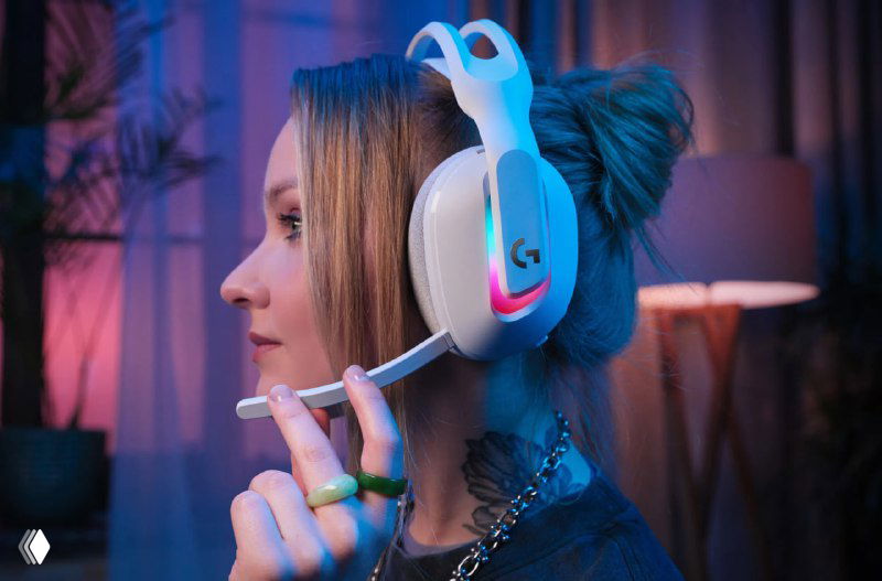 Портрет девушки в белых наушниках Logitech с выдвижным микрофоном и RGB-подсветкой; видно посадку и дизайн гарнитуры в профиле.
