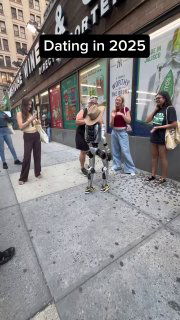 Робот идёт по тротуару рядом с молодыми людьми; на фото видна наклейка «Dating in 2025», витрины и городская улица с прохожими.