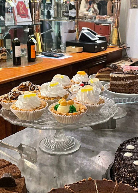 Витрина с десертами: тарты и пирожные на стеклянной подставке у кассы столовой, демонстрирующие выбор сладкого после обеда