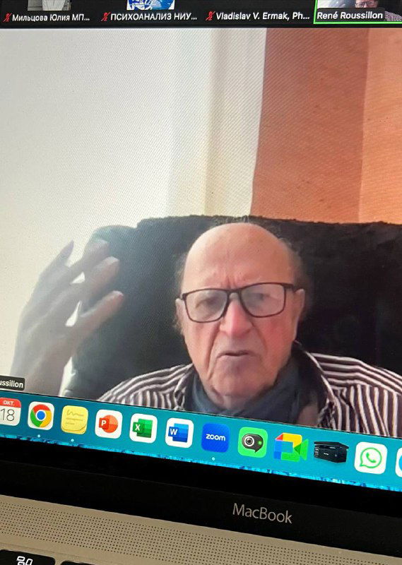 Скриншот с видеовстречи: Рене Руссийон в очках объясняет жестами, виден верх ноутбука MacBook с доком.