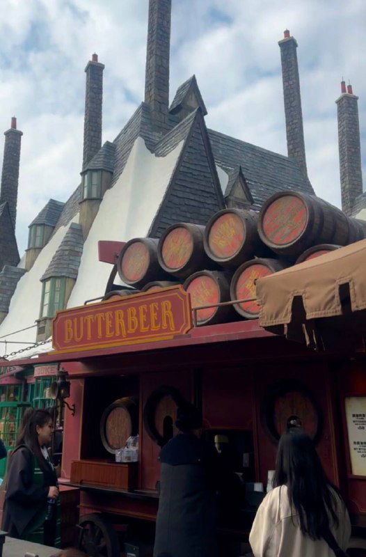 Ларёк с надписью Butterbeer и деревянные бочки, торговая точка в зоне Гарри Поттера в Universal Studios, посетители в очереди.