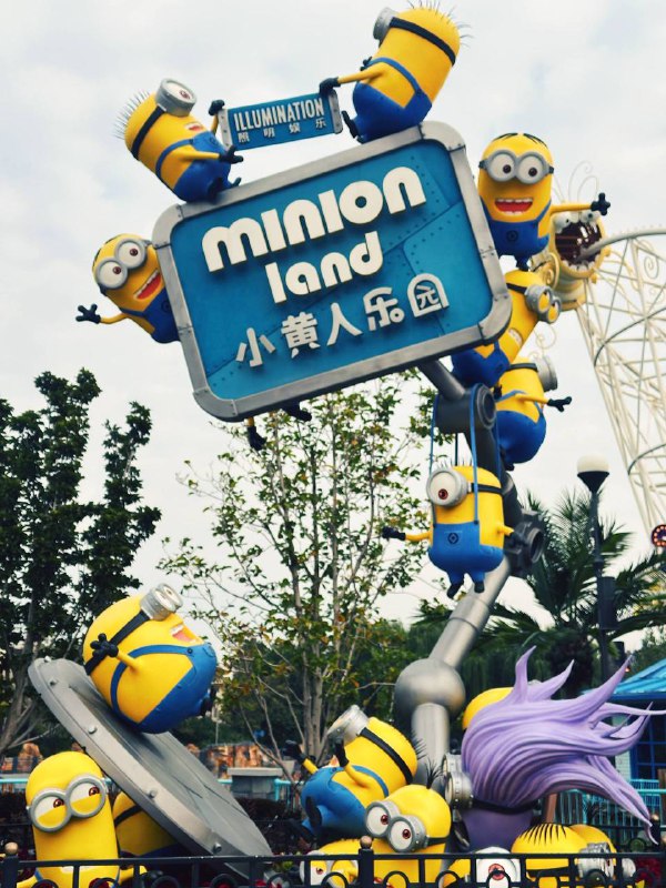 Яркая вывеска Minion Land с фигурками миньонов и посетителями; семейная зона парка развлечений Universal Studios в Пекине.