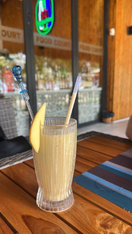 Освежающий тропический коктейль в высоком стакане с трубочкой и долькой лимона на столе кафе у моря — классическая летняя подача напитка.