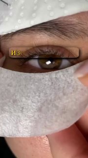 Крупный план глаза с патчем; мастер показывает изоляцию ресницы перед наращиванием, видны натуральные ресницы.