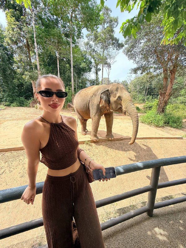 Автор позирует в солнечных очках и коричневом костюме у ограды, за ней слон — финальный кадр прогулки по сафари на Фукуоке.