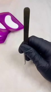 Черные перчатки держат пинцет для наращивания ресниц на фоне фиолетовой палитры — кадр из видео с демонстрацией упражнений.