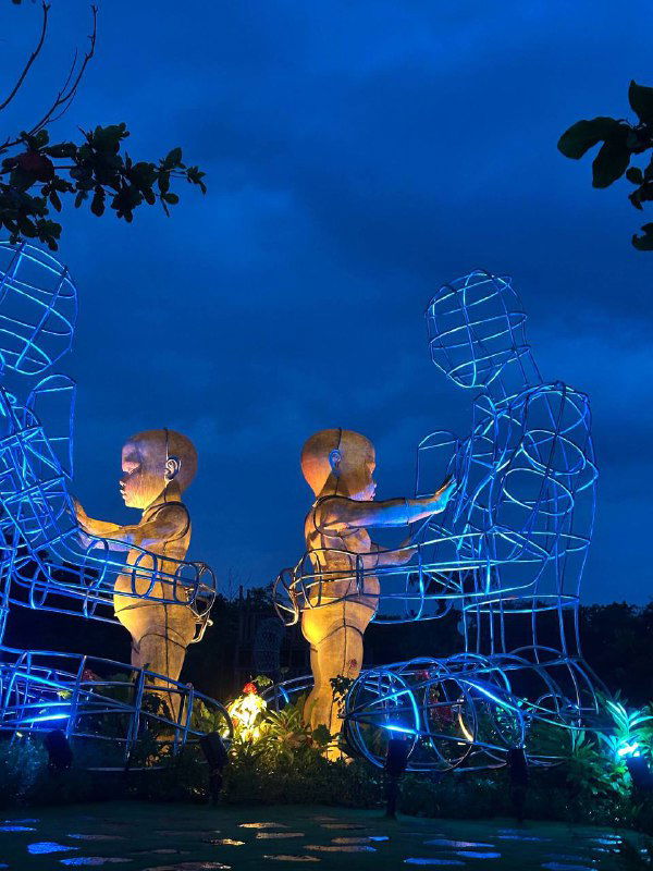 Ночная фотография светящихся скульптур и неба: синие подсветки, декоративные инсталляции и вечерняя прогулка туристов.