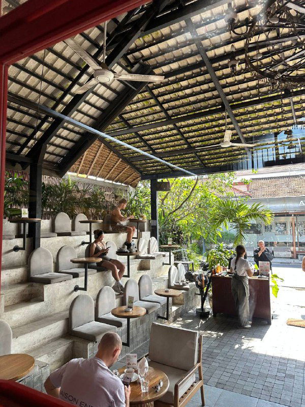 Открытое кафе с террасой и ступенчатой зоной для сидения, зеленью и посетителями — пространство для отдыха и работы в поездке.