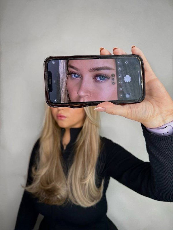 Фото мастера, держащей смартфон с портретом клиента в кадре — идея сторис/фото для показа результата и процесса работы в профиле.