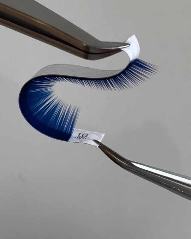 Пучок цветных (синих) ресниц, подвешенный пинцетом на нейтральном фоне — нестандартный визуальный элемент для разнообразия контента.