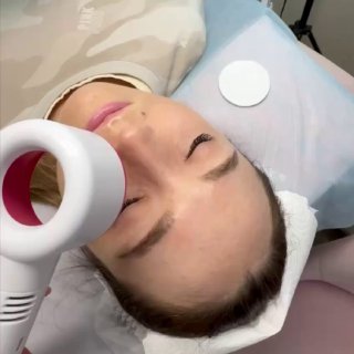 Крупный план клиентки во время процедуры наращивания ресниц: она лежит с закрытыми глазами, рядом лампа и инструменты мастера в салоне.