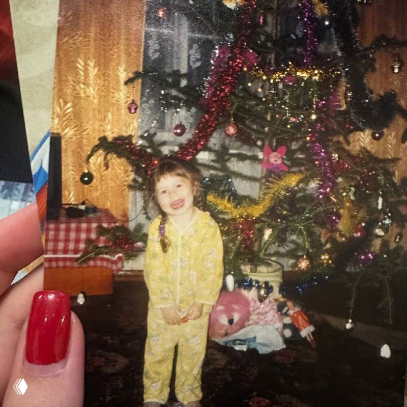 Детская фотография у новогодней ёлки: маленькая девочка в пижаме улыбается, семейное воспоминание из праздничных лет детства автора.