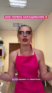 Ведущая в розовом фартуке и солнцезащитных очках в салоне рассказывает о своём первом наращивании ресниц — кадр из вертикального видео.