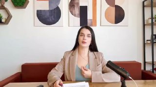 Женщина-лектор в кабинете сидит за столом с микрофоном и бумагами на столе, на заднем плане декоративные постеры — превью к видео о подготовке.