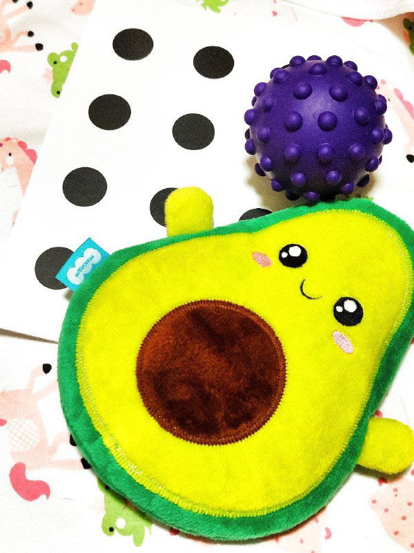 Мягкая игрушка в виде авокадо и фиолетовый массажный мячик на развивающем коврике — примеры первых тренажёров и тактильных материалов для ребёнка.