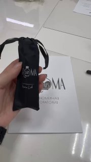 Рука держит небольшой чёрный мешочек с логотипом парфюмерии на фоне рабочего стола мастер‑класса — упаковка для пробника аромата.
