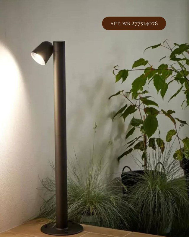 Столбовой садовый светильник на высокой стойке, направленный вниз — пример уличного освещения рядом с растениями и дорожками.