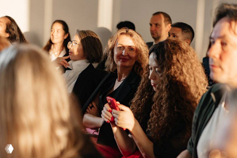 Аудитория конференции по медиации: слушатели в зале, женщина с телефоном в кадре, мягкое боковое освещение и деловая атмосфера мероприятия.